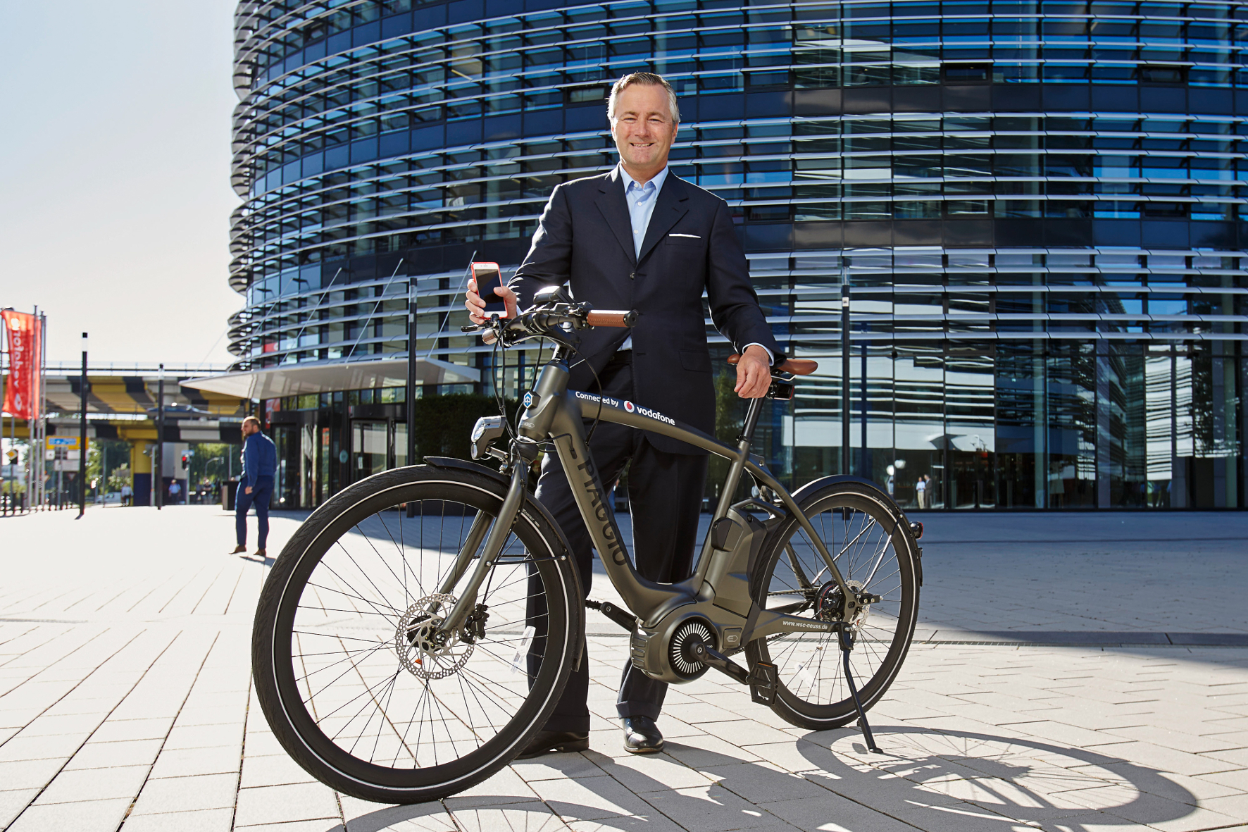 Mann im Anzug mit Elektro-Bike vor Vodafone Gebäude in Düsseldorf