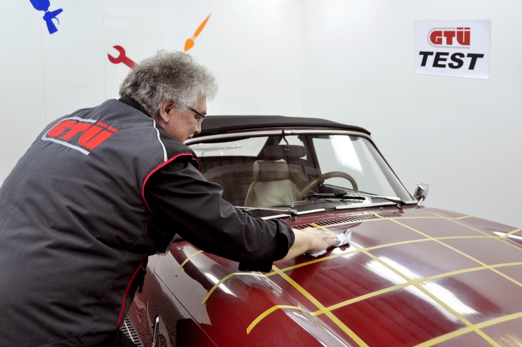 Mann im Kittel steht schräg neben Auto und trägt Politur auf