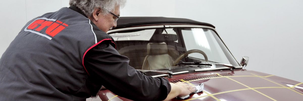 Mann im Kittel steht schräg neben Auto und trägt Politur auf