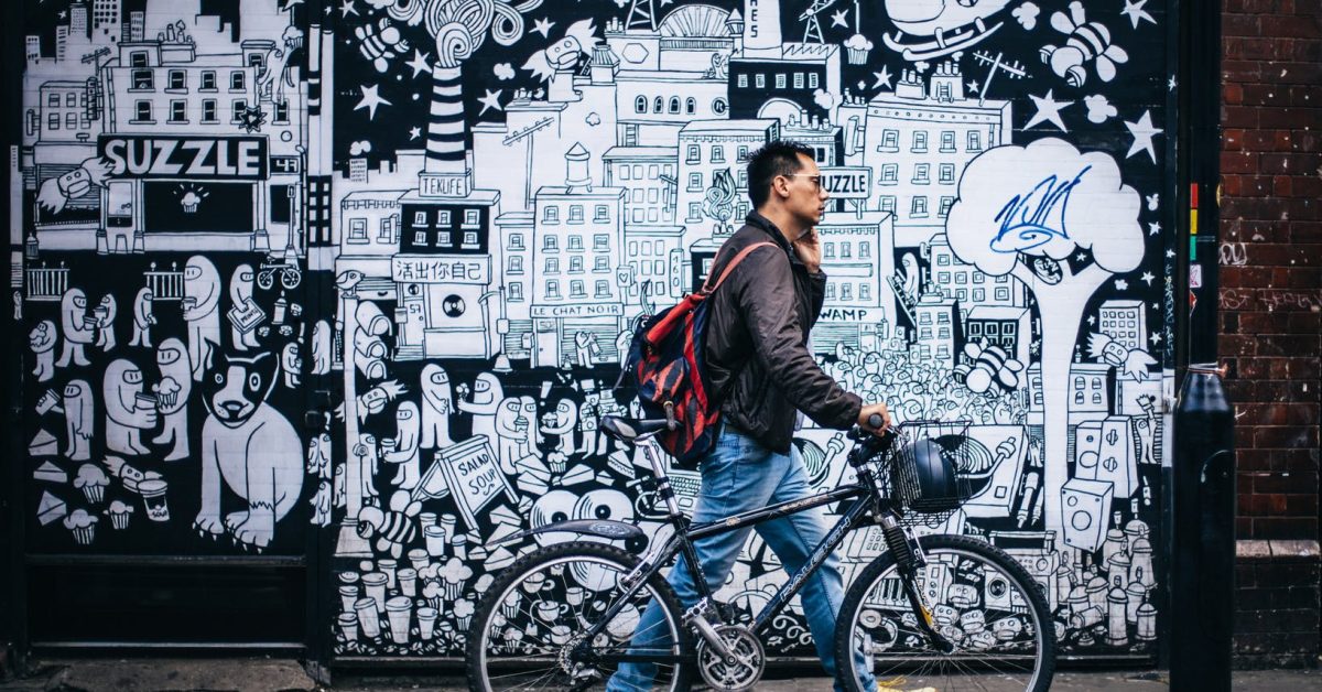 Mann schiebt Fahrrad vor einer Grafitti Wand