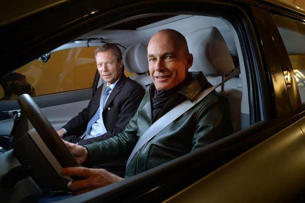 Zwei Männer in einem roten Auto blicken durch die Scheibe der Fahrertür.