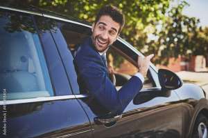 Im on my way to work buddy. Shot of a cheerful young businessman hanging out of a car window and pointing with his hand towards the front of his car.
