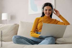 Woman with laptop and headphones sitting on sofa at home