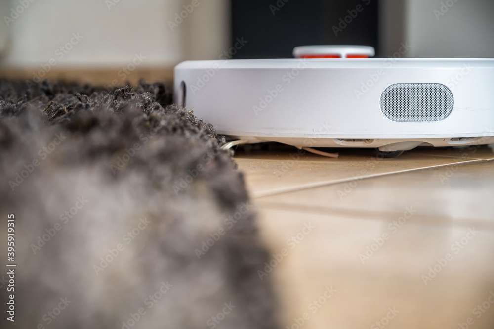 Moderner Saugroboter saugt einen Fliesenboden, bleibt aber an der Teppichkante hängen