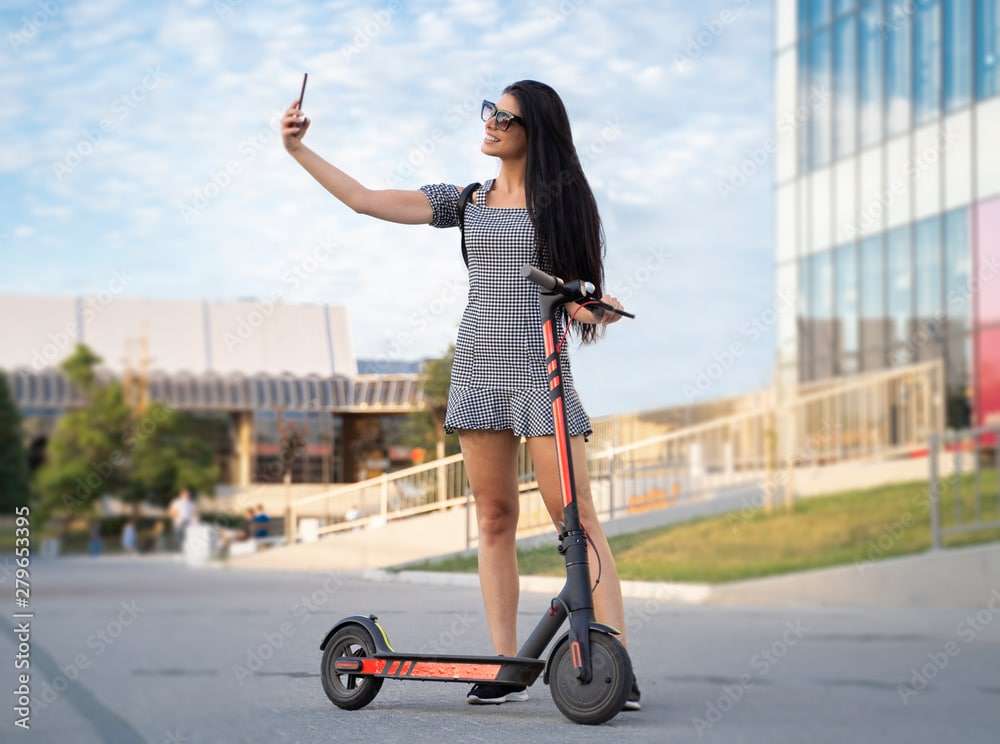 Attractive young woman taking selfie next to electric scooter