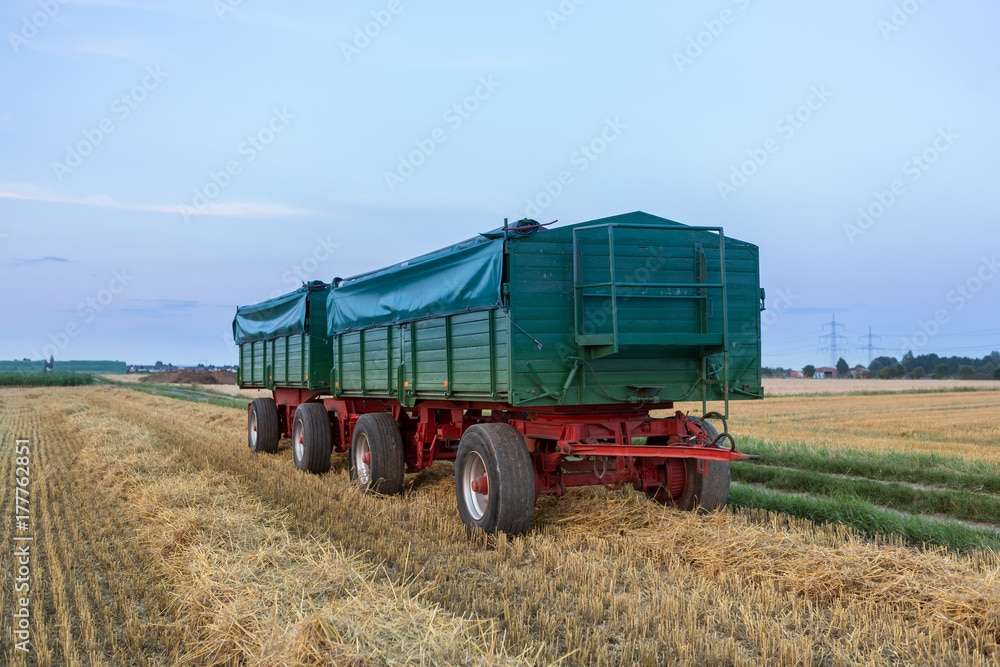 Grüner Landwirtschaftsanhänger abgedeckt mit einer Plane, beladen mit geerntetem Gut im Feld